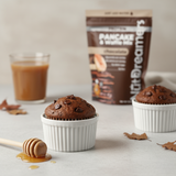 Chocolate muffins in white ramekins with a glass of coffee and a package of Nut Dreamers Chocolate Pancake & Waffle Mix in the background.