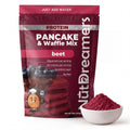 A stand-up pouch of NutDreamers Protein Pancake & Waffle Mix in beet flavor, shown next to a small white bowl filled with the red powder. The packaging is dark red with white and silver text and a graphic of pancakes with blueberries.