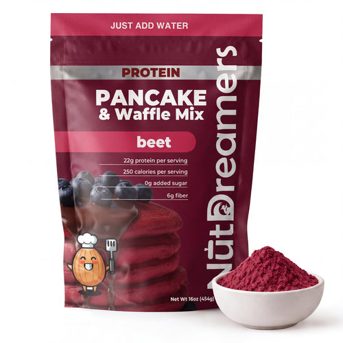 A stand-up pouch of NutDreamers Protein Pancake & Waffle Mix in beet flavor, shown next to a small white bowl filled with the red powder. The packaging is dark red with white and silver text and a graphic of pancakes with blueberries.