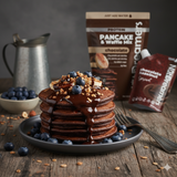 Stack of chocolate pancakes with blueberries and nuts on a plate, with Dreamery Pancake & Waffle Mix in the background.