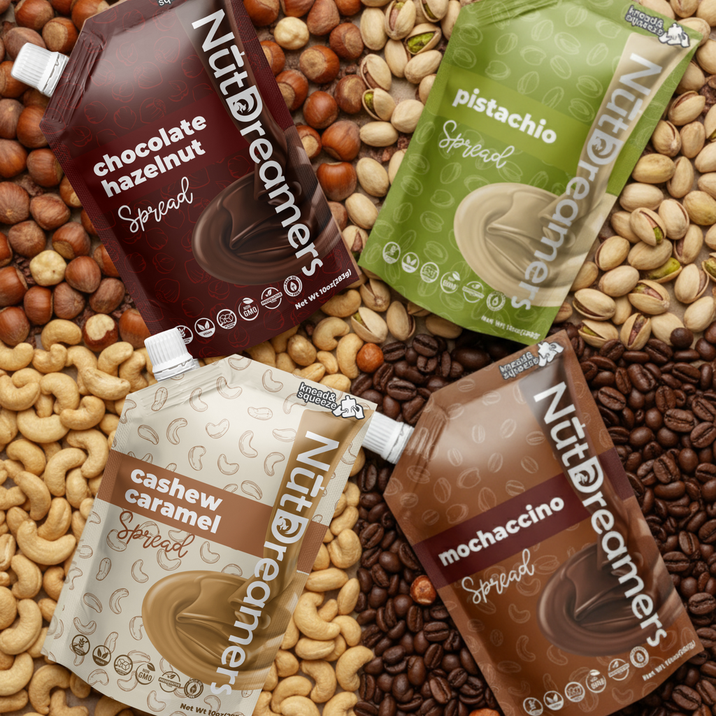Four packets of NutDreamers spreads on a background of nuts and coffee beans.