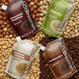 Four packets of NutDreamers spreads on a background of nuts and coffee beans.
